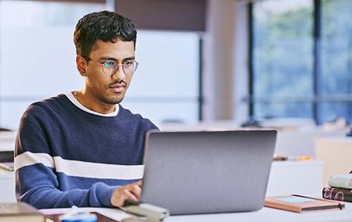 A male student studies on a laptop in a sunny room